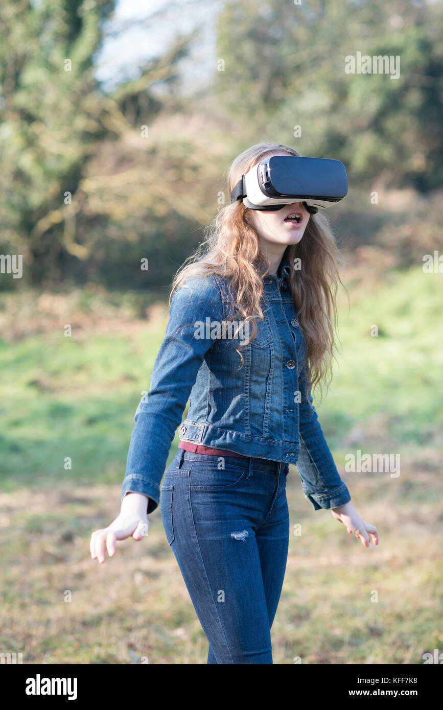 teenage girl dressed in denim in sunshine wearing virtual reality headset outdoors Stock Photo