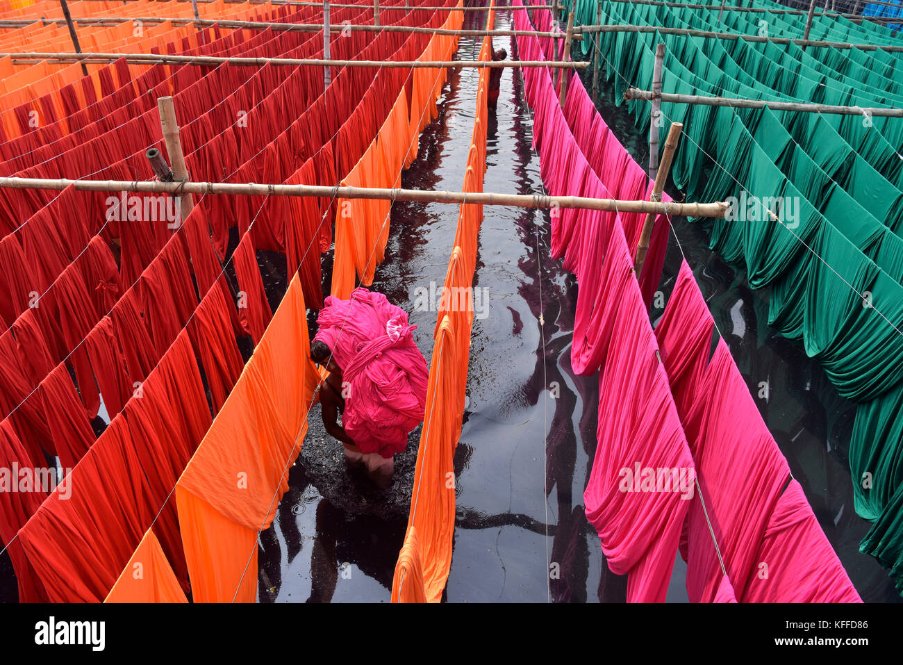 A Bangladeshi worker carries Garments fabric after dries them under the sun at Narayanganj, near Dhaka, Bangladesh. Knitting is the manufacturing stage that converts yarn into fabric through the process of interlocking loops. Weaving is the process of fabric formation in which yarns are interlaced at right angles using a weaving machine (loom) - different patterns can be produced by passing each sideways ''weft'' yarn under or over a varying number of lengthways ''warp'' threads, forming the weave. Stock Photo