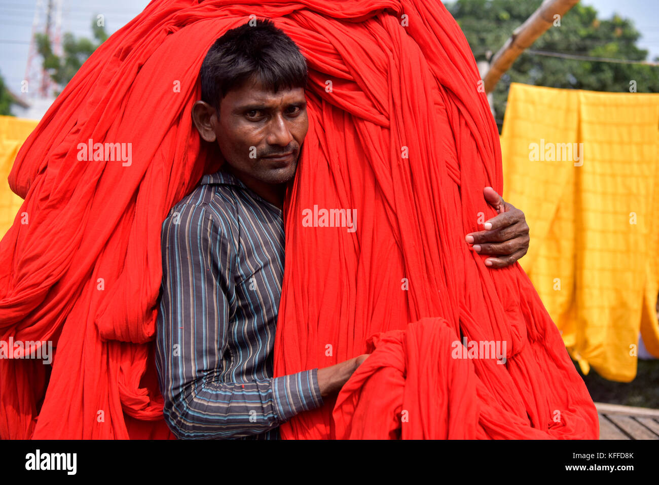 A Bangladeshi worker carries Garments fabric after dries them under the sun at Narayanganj, near Dhaka, Bangladesh. Knitting is the manufacturing stage that converts yarn into fabric through the process of interlocking loops. Weaving is the process of fabric formation in which yarns are interlaced at right angles using a weaving machine (loom) - different patterns can be produced by passing each sideways ''weft'' yarn under or over a varying number of lengthways ''warp'' threads, forming the weave. Stock Photo