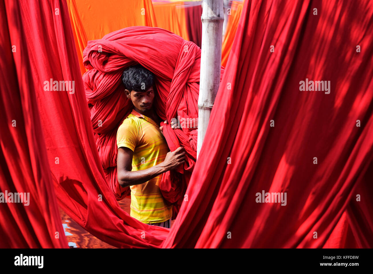 A Bangladeshi worker carries Garments fabric after dries them under the sun at Narayanganj, near Dhaka, Bangladesh. Knitting is the manufacturing stage that converts yarn into fabric through the process of interlocking loops. Weaving is the process of fabric formation in which yarns are interlaced at right angles using a weaving machine (loom) - different patterns can be produced by passing each sideways ''weft'' yarn under or over a varying number of lengthways ''warp'' threads, forming the weave. Stock Photo