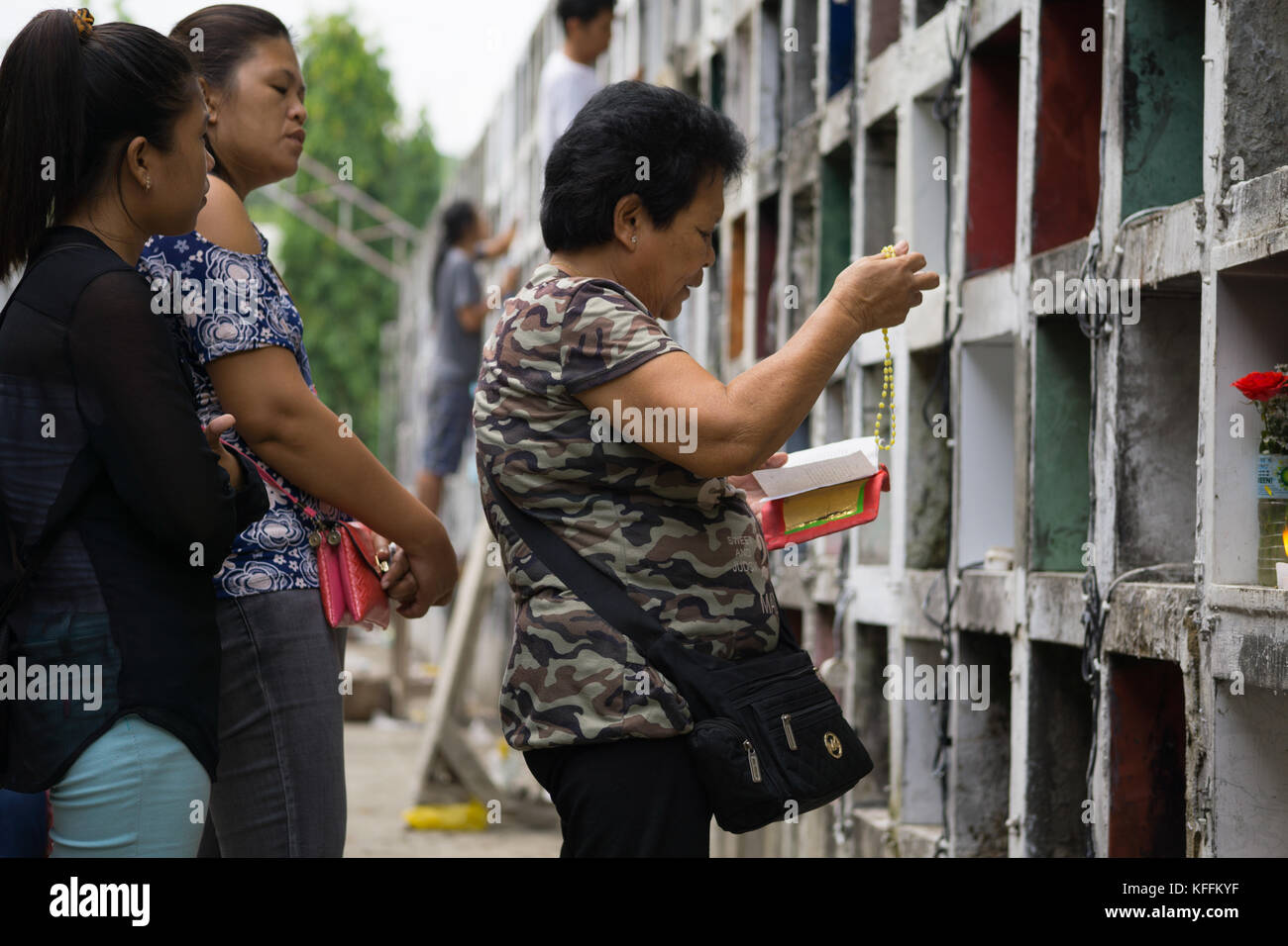 Carreta Cemetery, Cebu City, Philippines. 28th October, 2017. A family stand before a tomb of a loved one as a woman recites a prayer whilst holding Rosary Beads.All Saints day & All Souls day falling on the 31st October & 1st November respectively will see millions of Filipinos attending cemeteries across the country to remember deceased relatives & loved ones. Credit: imagegallery2/Alamy Live News Stock Photo