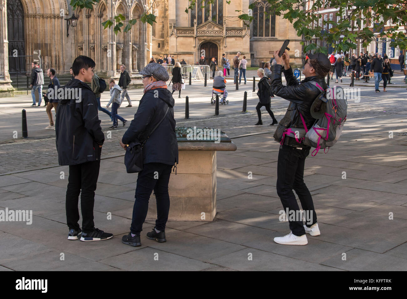 Man takes photo with phone as tourists stand in York centre piazza by model of Minster area, cathedral & people beyond - North Yorkshire, England, UK. Stock Photo