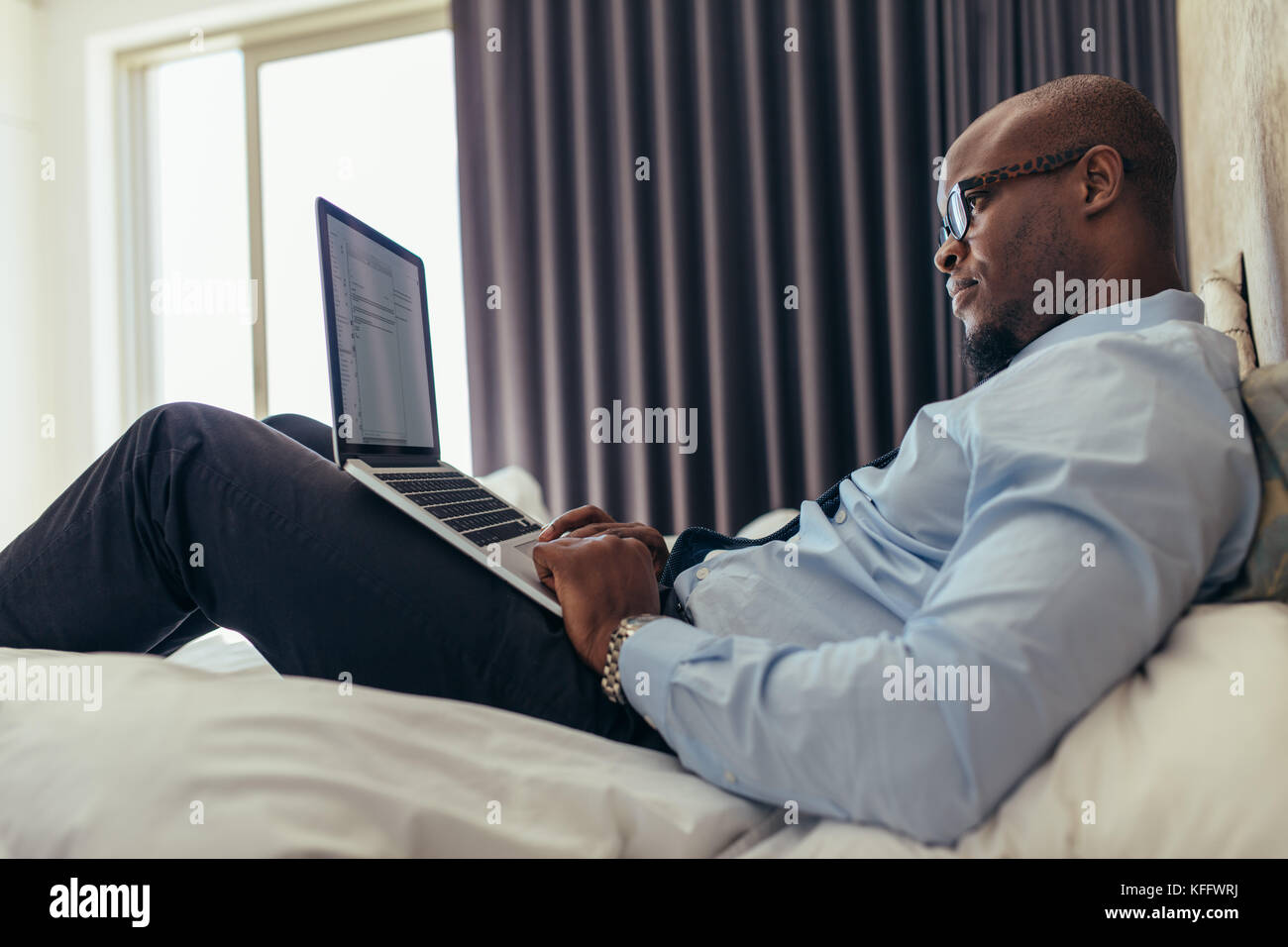 Man in formal clothes working on laptop while lying in bed. Businessman ...