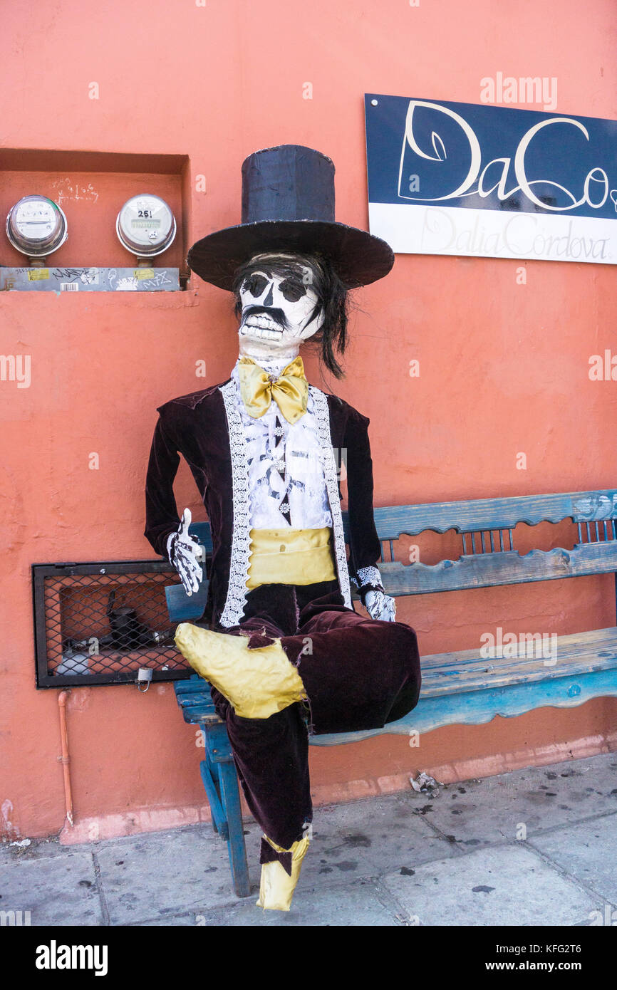 jaunty life size Day of the Dead gentleman with repaired plaster head hands & chipped top hat sits outside shop in tacky velvet & lace formal attire Stock Photo