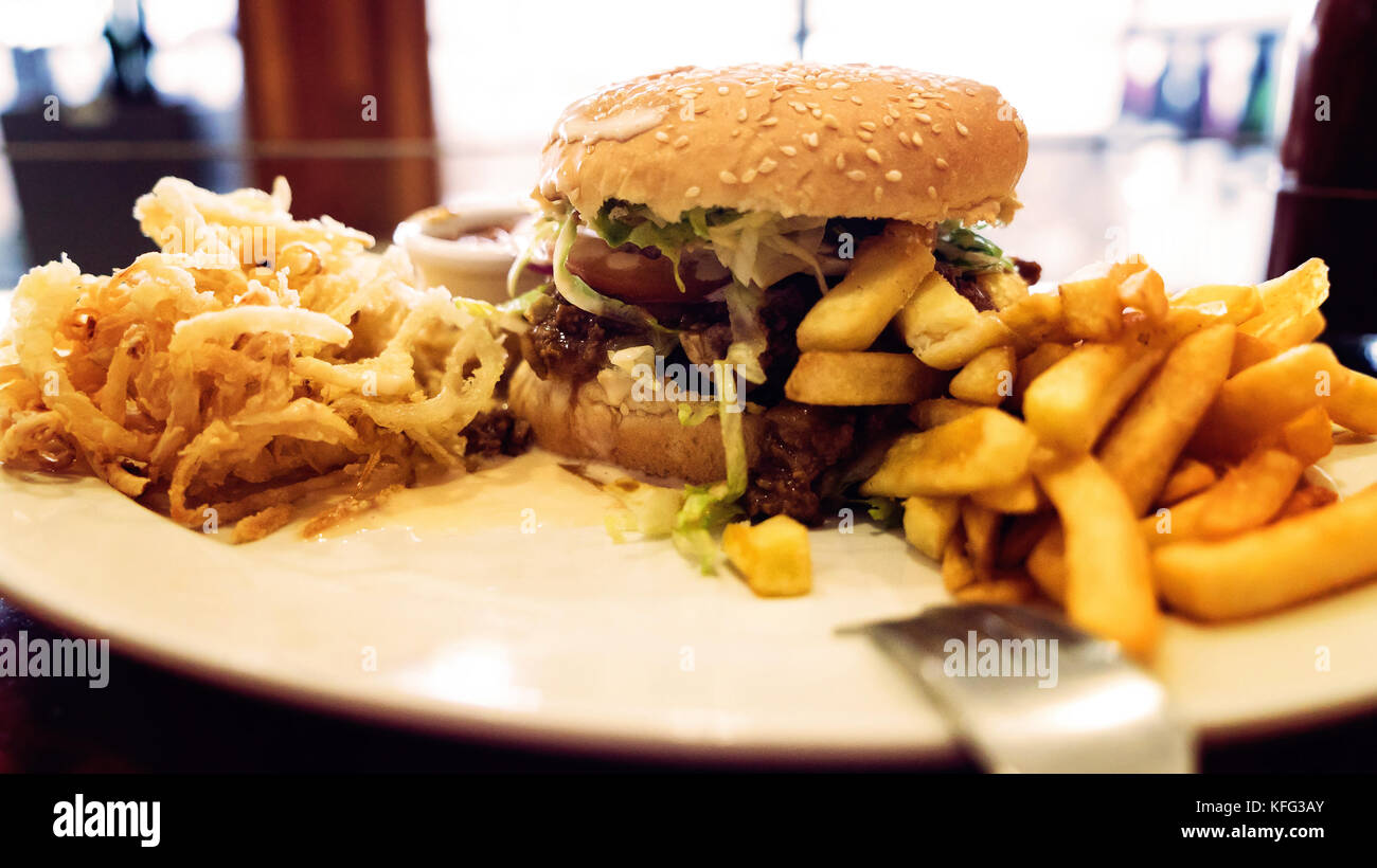 Unhealthy meal with mexican nacho chips, beef burger, loaded with cheese, fries, onion rings Stock Photo