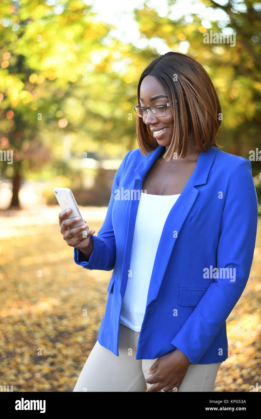 A strong young black women using a smartphone in a park during fall Stock Photo