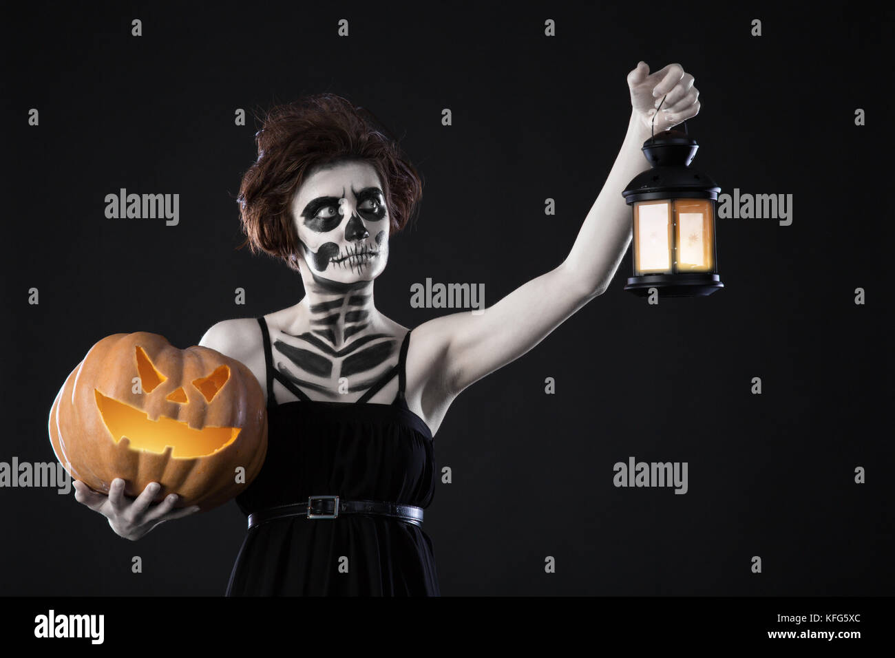 Happy Halloween. Portrait of black witch with scary makeup over black background. Holding pumpkin and lamp in hands. Holiday Stock Photo