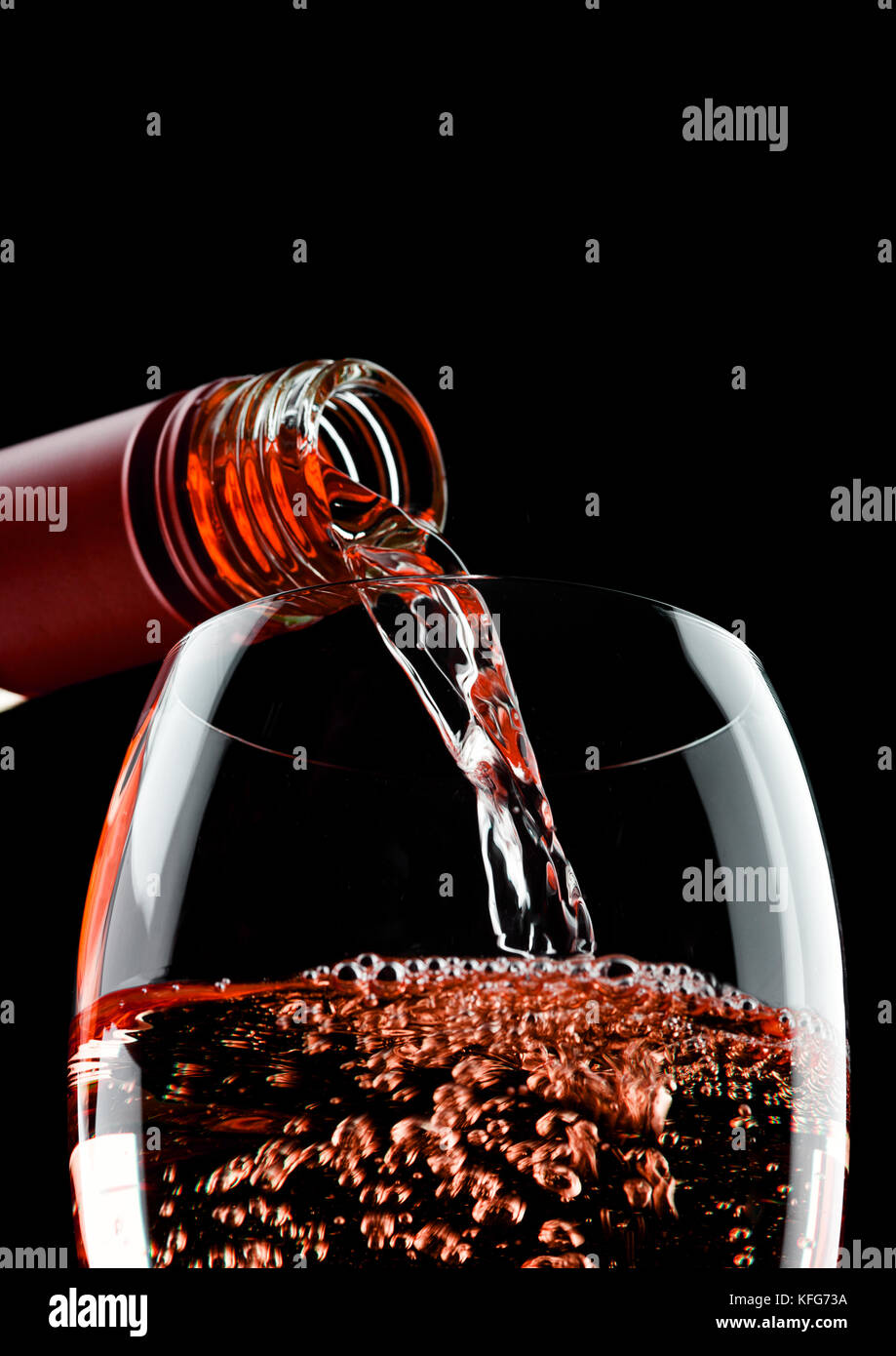 Pouring rose pink wine from bottle to glass isolated on black ...