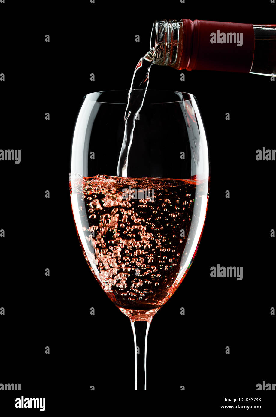 Pouring rose pink wine from bottle to glass isolated on black ...