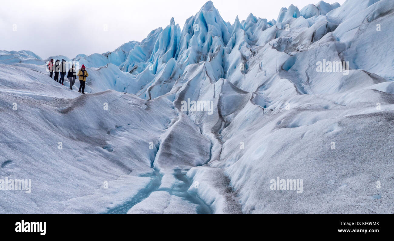 Guides leading a group of colorfully dressed tourists on a short glacier hike with blue sky, glacial landscapes, running streams and glacial peaks Stock Photo