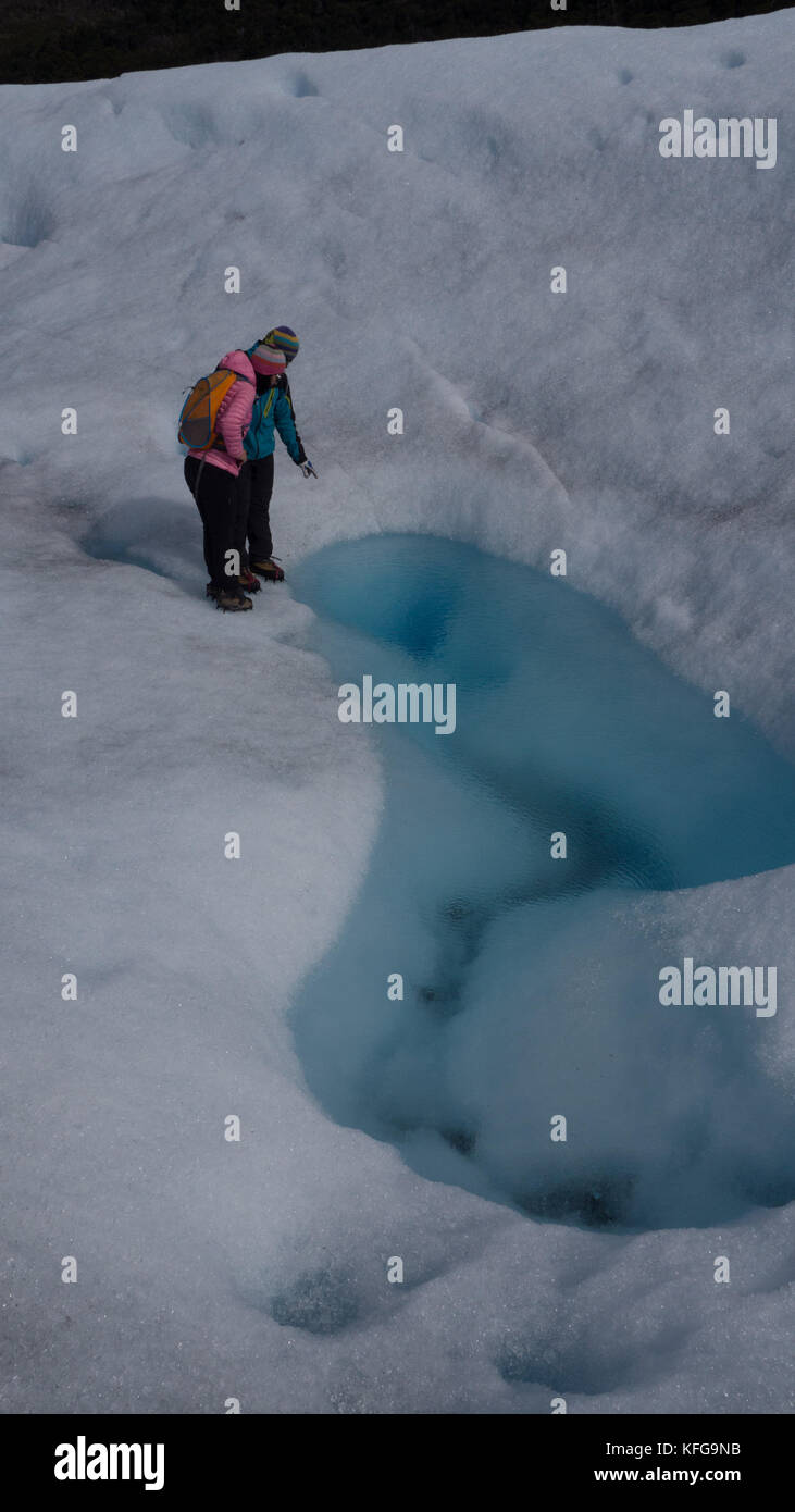 Glacier guide pointing to glacial pool that forms nightly on surface of glacier to a pinked coated female tourist on short hiking tour. Stock Photo