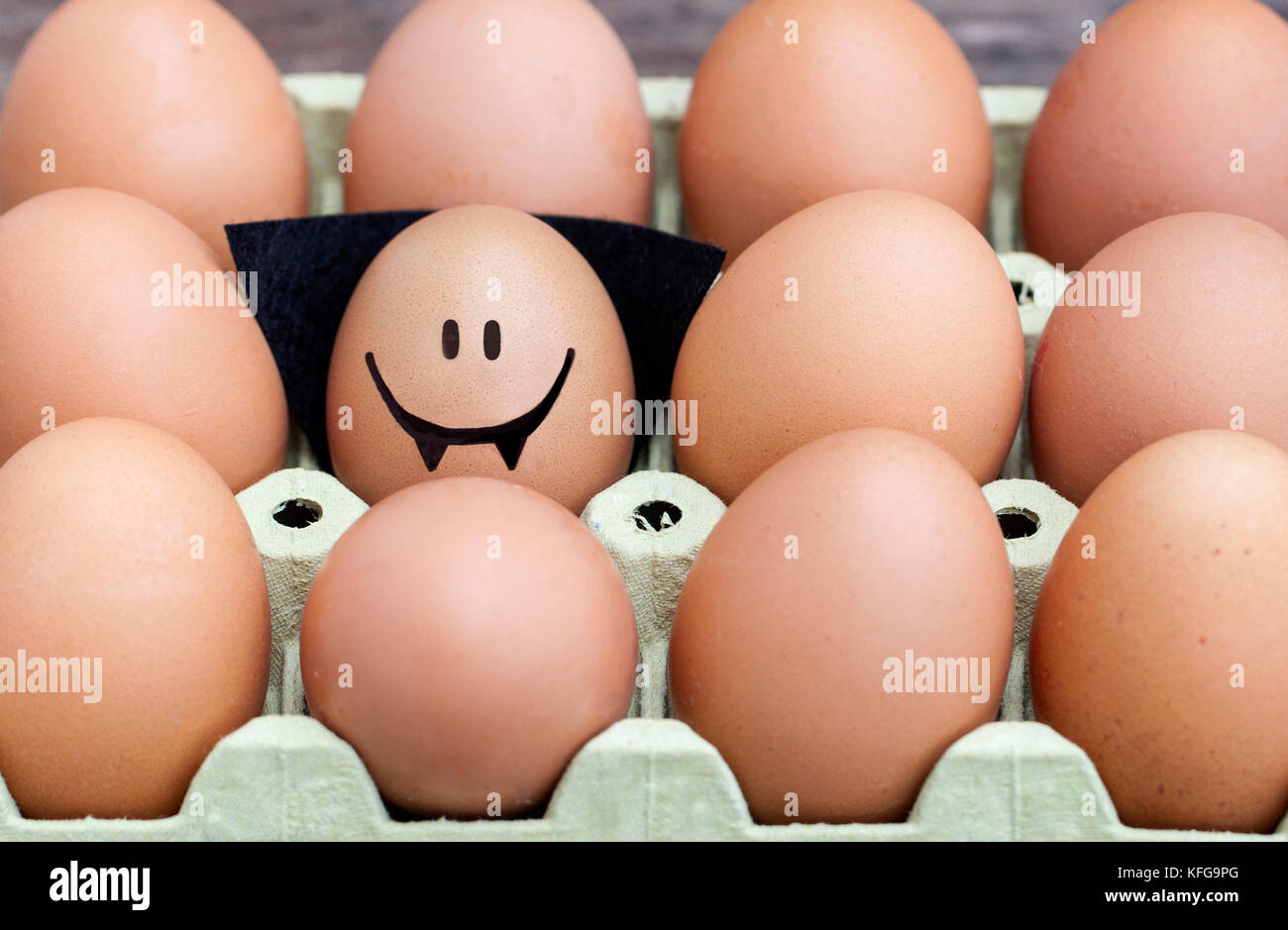 Smiling egg  dressed up as a vampire wearing souronded by blank brown eggs. Stock Photo