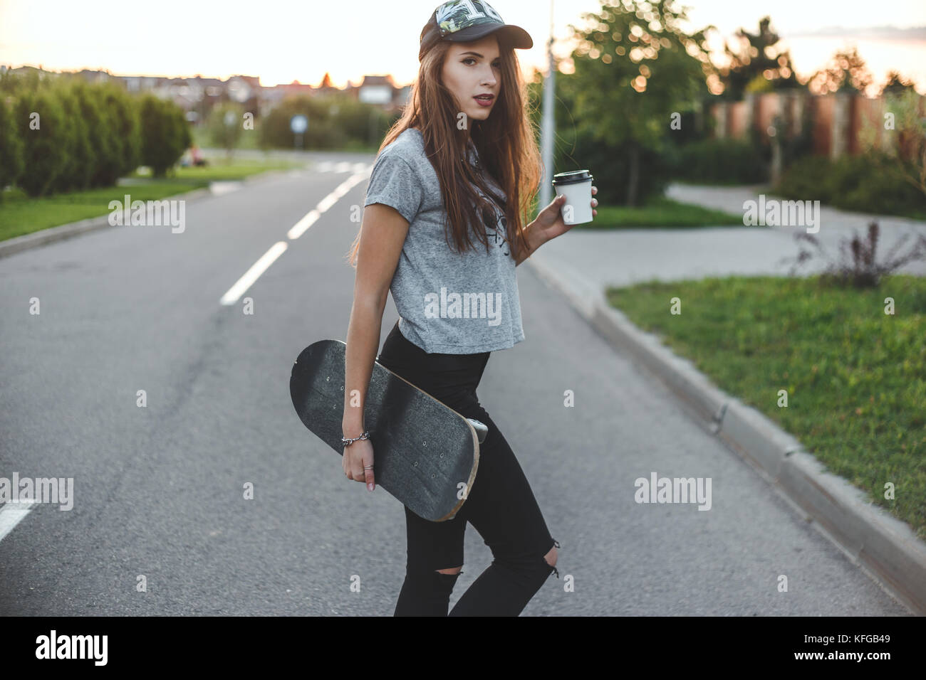 skater girl with coffee cup in front of the sun starts her day. Stock Photo