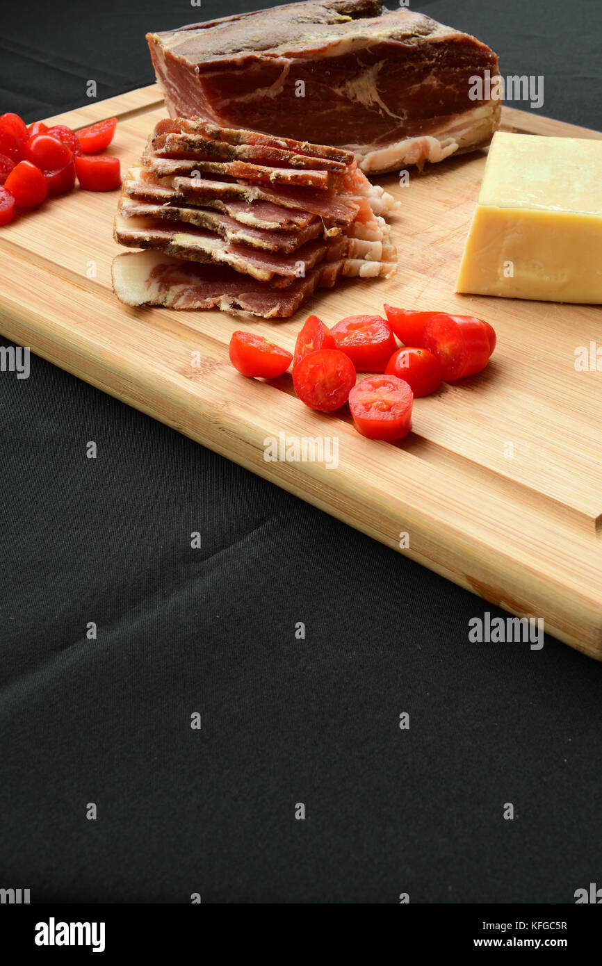 Cheese, Bacon and cherry tomatoes on cutting board Stock Photo