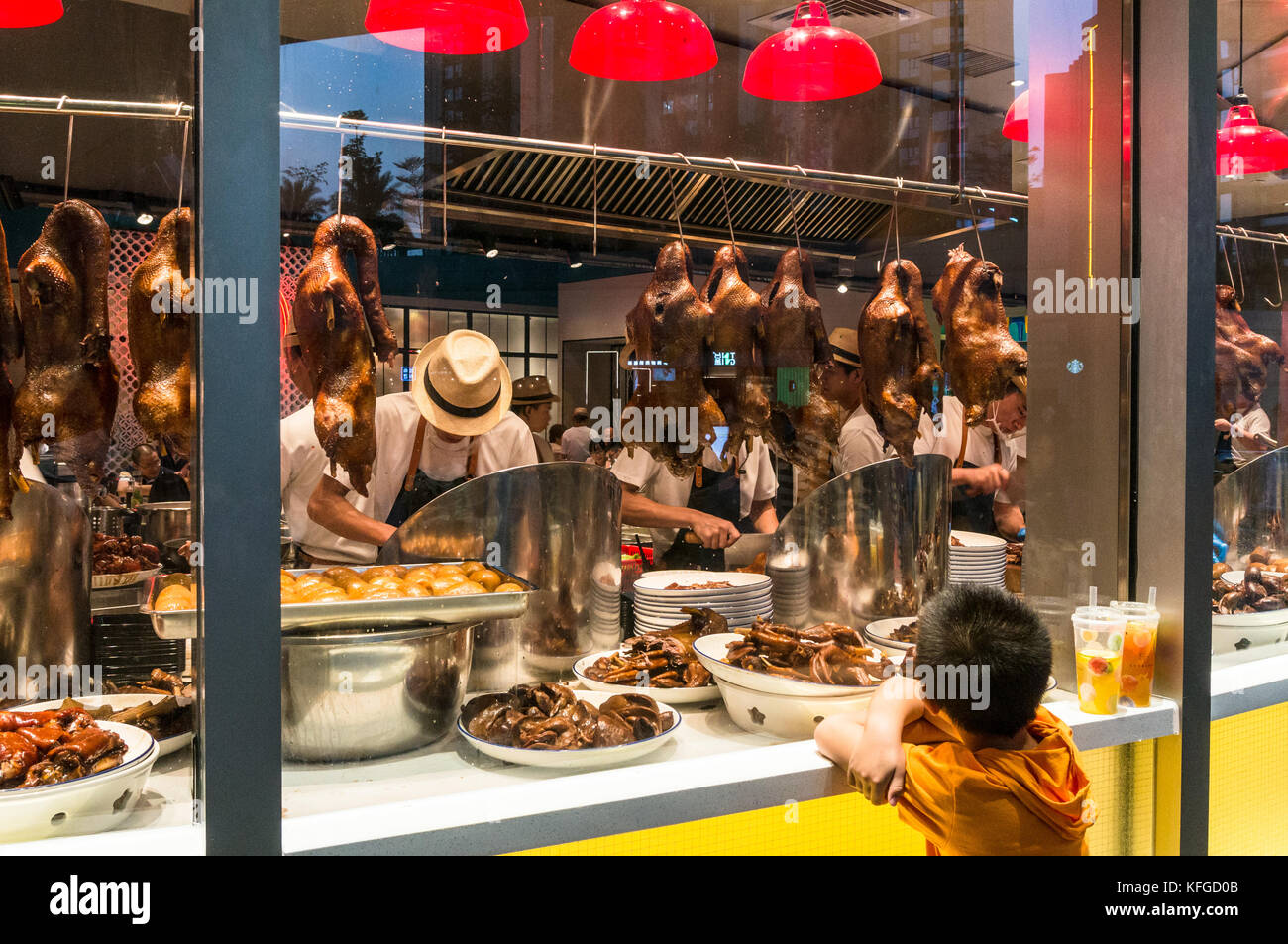 Roasted ducks hanging in window as boy watches at a restaurant in