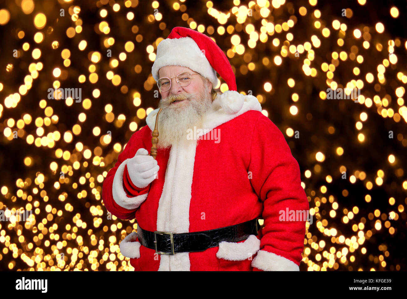 Santa Claus with pipe, portrait. Authentic Santa Claus with smoking pipe on New Year lights background. Stock Photo
