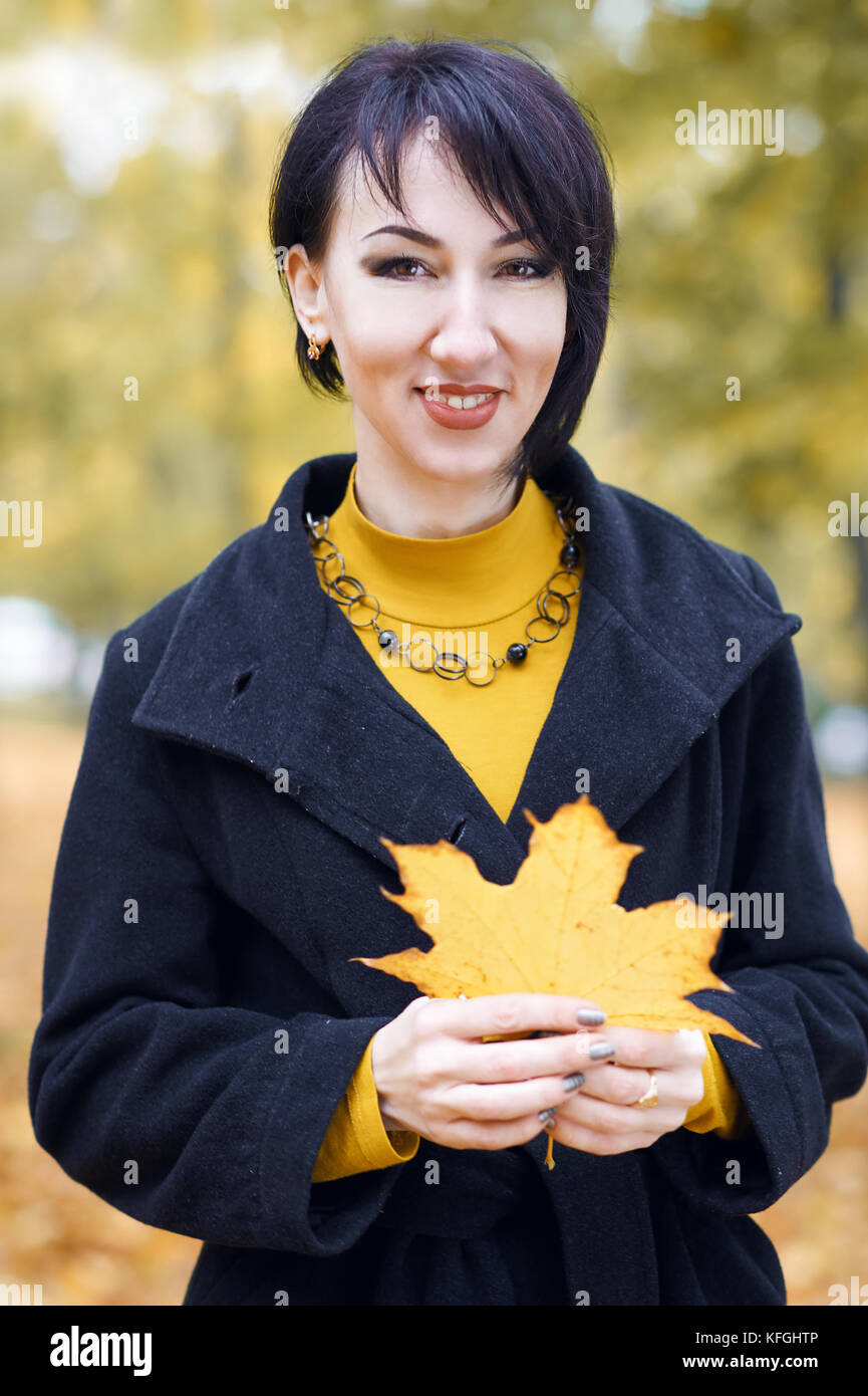 beautiful girl portrait with yellow leaf in hand, autumn city park on ...
