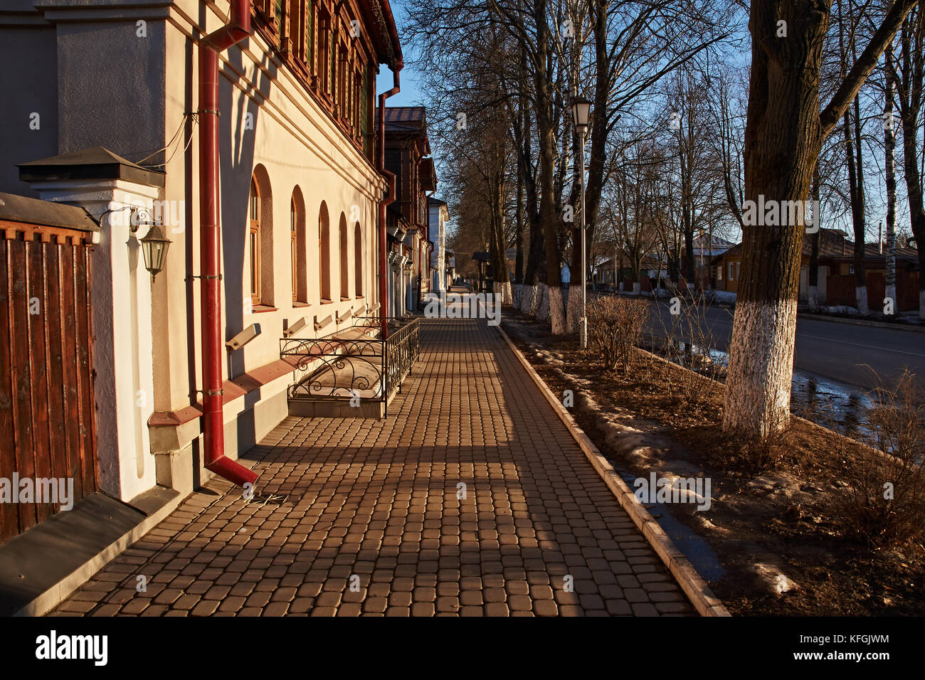 Low-rise buildings, The pavement is covered with tiles. The road is covered with asphalt. Between the road and the sidewalk grow trees.Suzdal.Golden Stock Photo