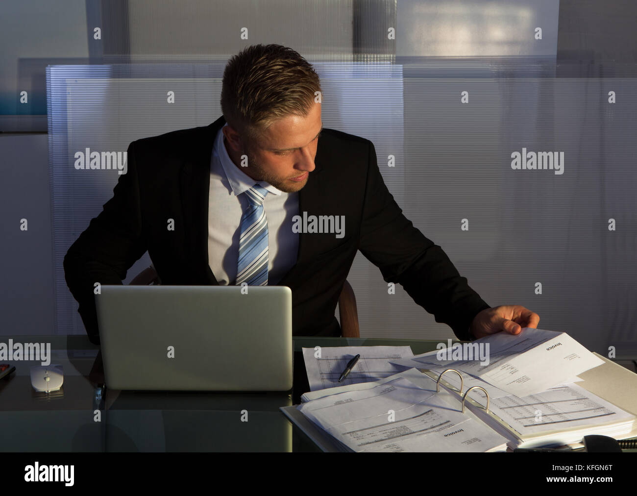 Businessman under pressure working overtime late into the evening sitting at his desk collating a report for a deadline in the morning Stock Photo