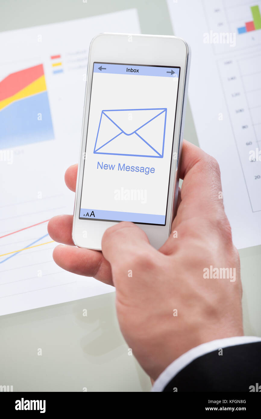 New email message icon on a mobile phone held in the hand of a businessman as he checks his mail at work Stock Photo