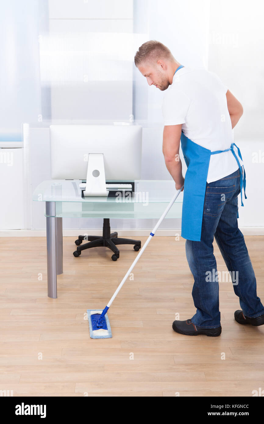 Handsome male janitor or cleaner cleaning the floor in an office building using a mop to wash the and disinfect the surface Stock Photo