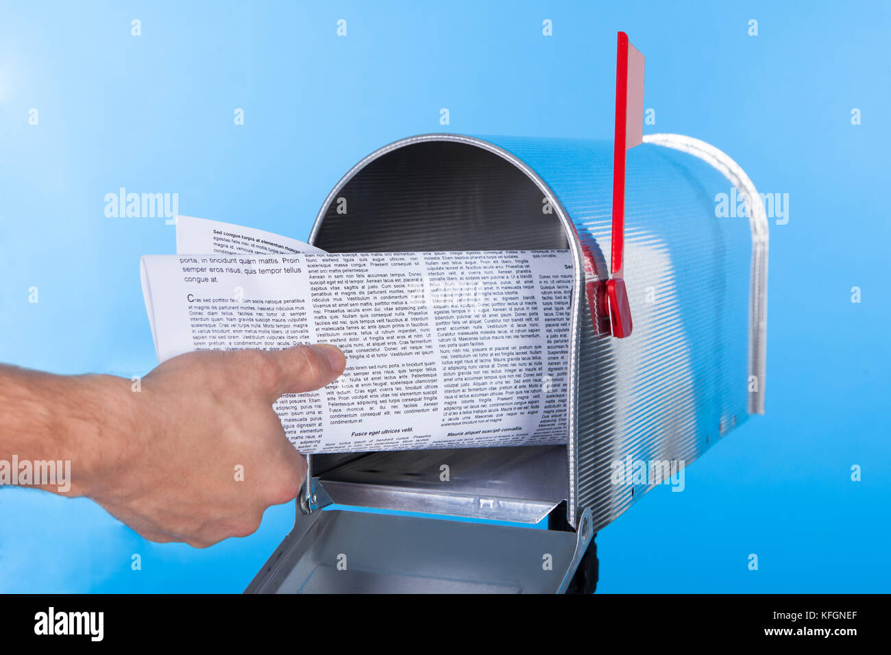 Man removing a newspaper from his mailbox with a closeup of his hand clasping the folded paper against a blue sky Stock Photo