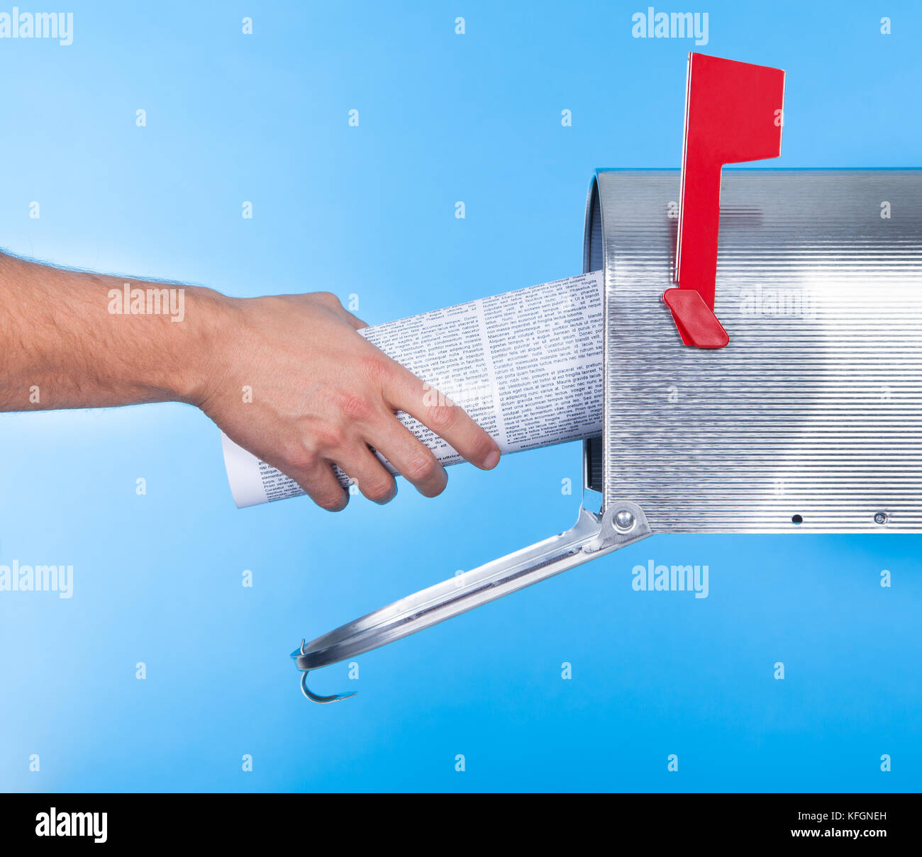 Man removing a newspaper from his mailbox with a closeup of his hand clasping the folded paper against a blue sky Stock Photo