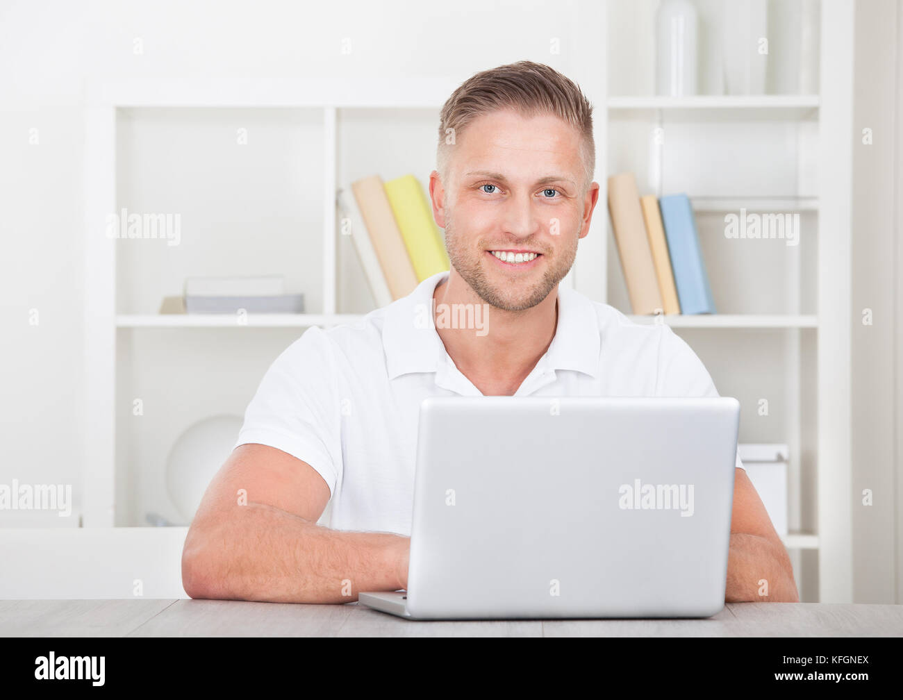 Smiling young man in a short sleeved shirt sitting working at home on a laptop in a home office Stock Photo