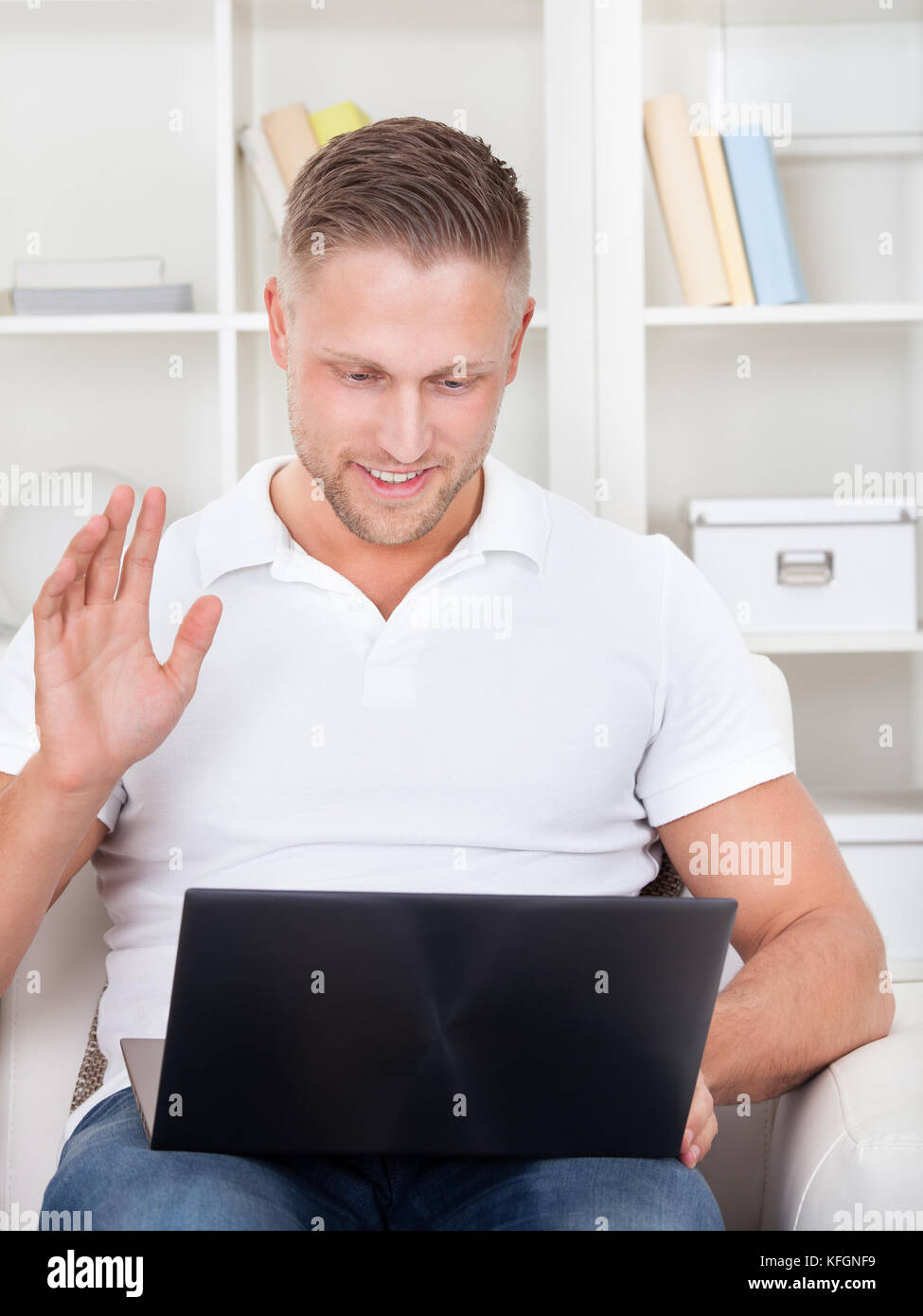 Businessman waving in pleasure to his laptop as he sits on a chair reading information on the screen Stock Photo