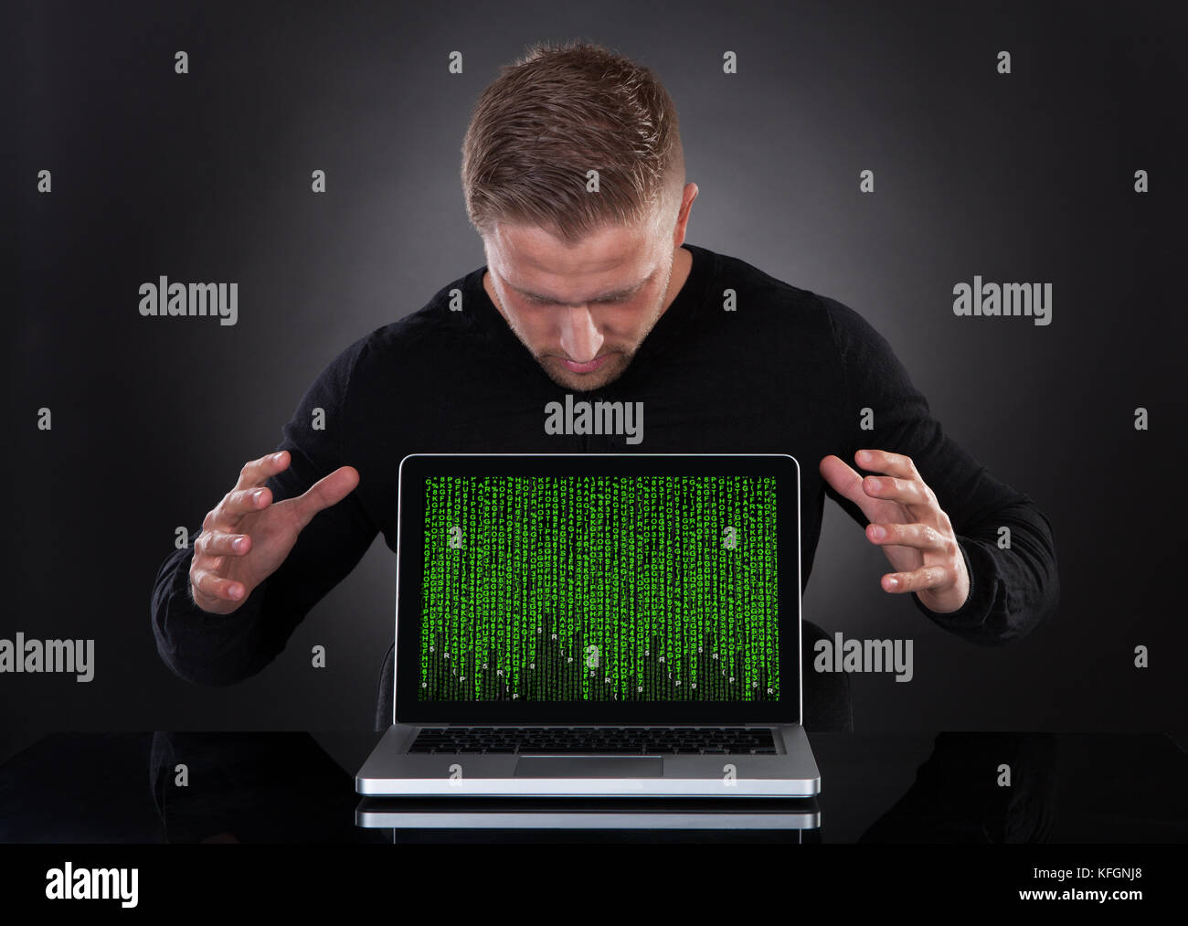 Man or hacker stealing data from a laptop at night bending forwards over the keyboard in the glow from the screen as he browses the internet or retrie Stock Photo
