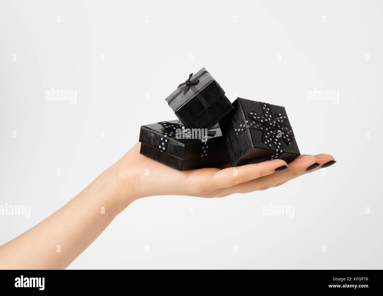 Female hand holding a three black gift-boxes on a palm. Isolated on white background. Shallow depth photo. Stock Photo