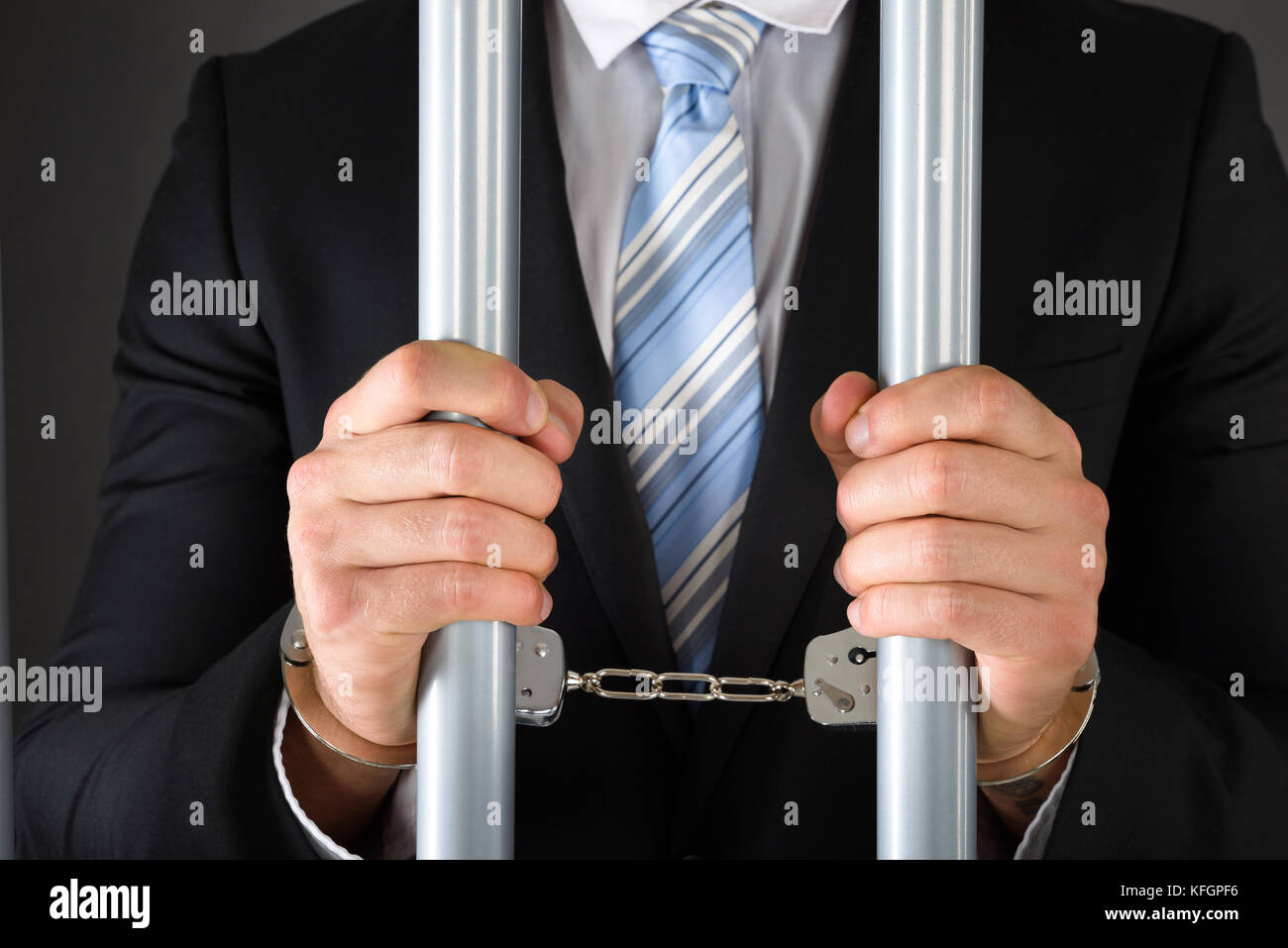 Close-up Of Handcuffed Businessman In Jail Holding Metal Bars Stock Photo