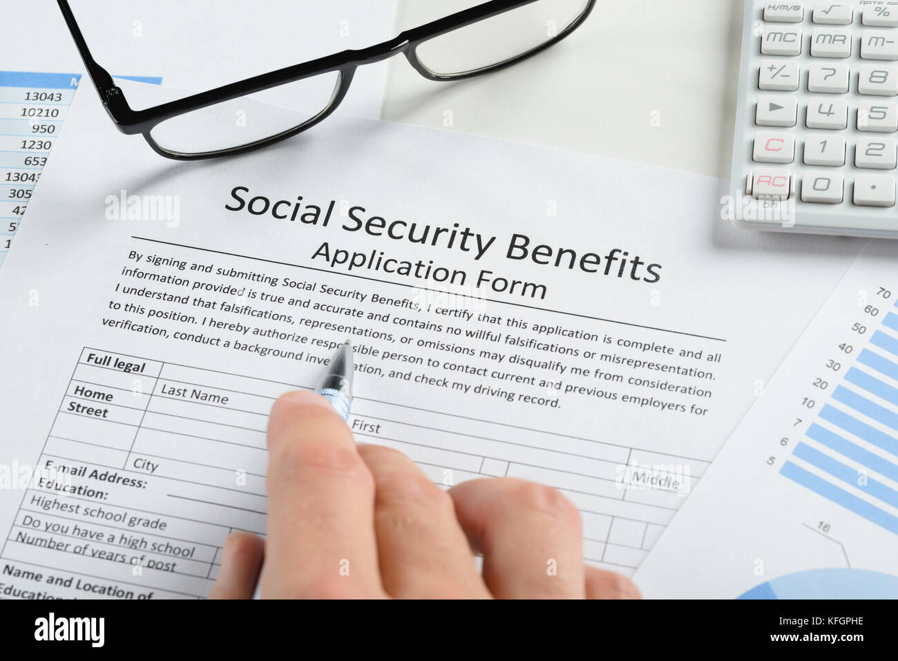 Close-up Of Hand With Pen And Eyeglasses Over Social Security Benefits Application Form Stock Photo
