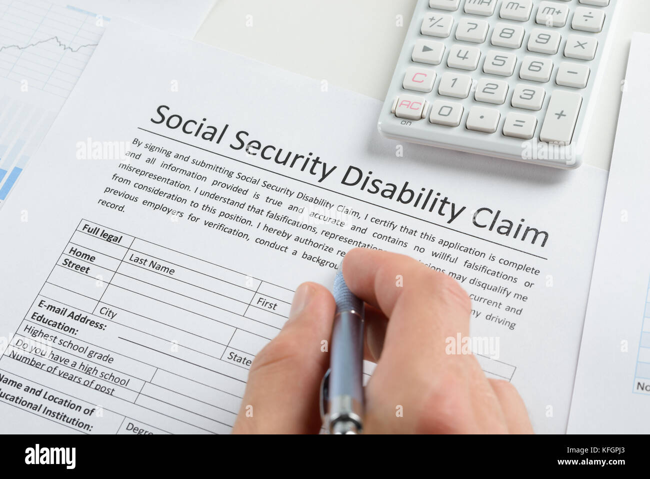 Close-up Of Person Hand With Pen And Calculator Filling Social Security Disability Claim Form Stock Photo