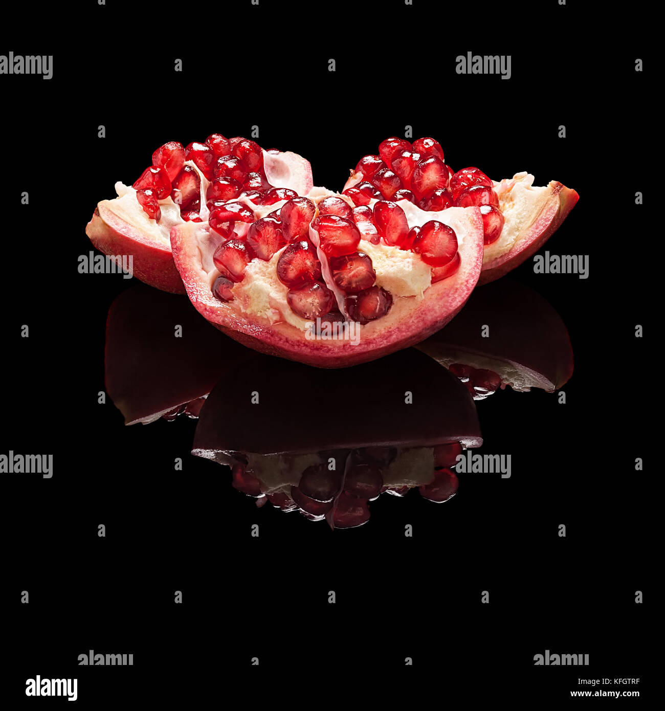Part of pomegranate fruit with seeds isolated on black glossy background with real reflection. Stock Photo