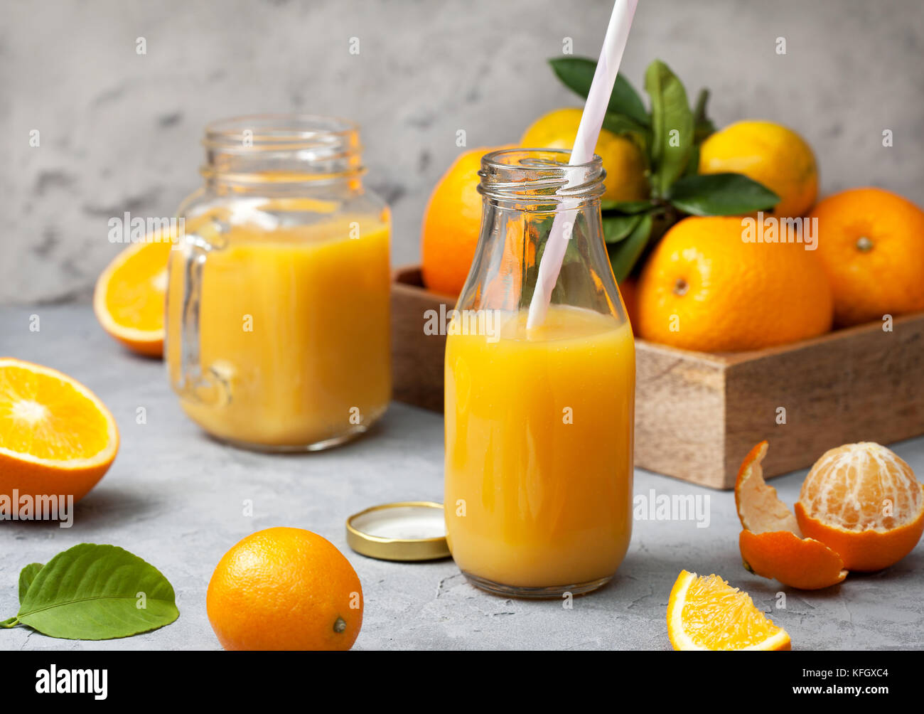 orange juice in glass bottles, fresh oranges and tangerines on a gray