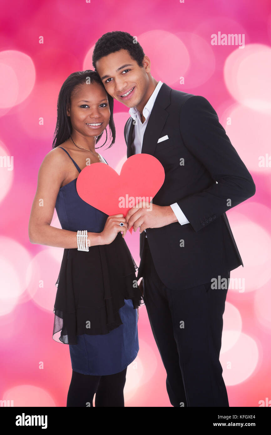 Portrait of happy couple holding paper heart over colored background ...