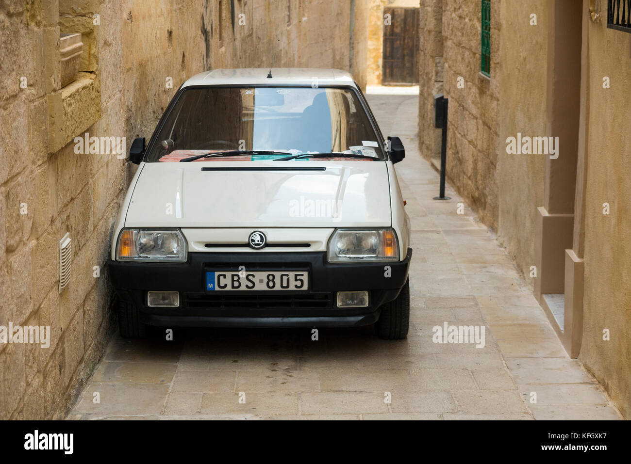 A Czechoslovakian Skoda car / vehicle parked too close to a wall in a narrow street / alley / road in the ancient walled city of Mdina in Malta. (91) Stock Photo