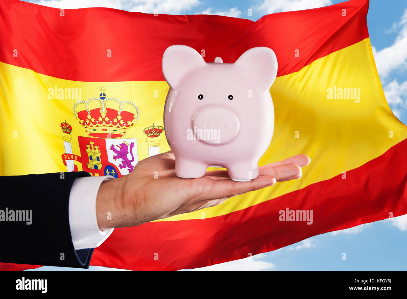 Businessman Holding Piggybank In Front Of Spanish Flag Stock Photo