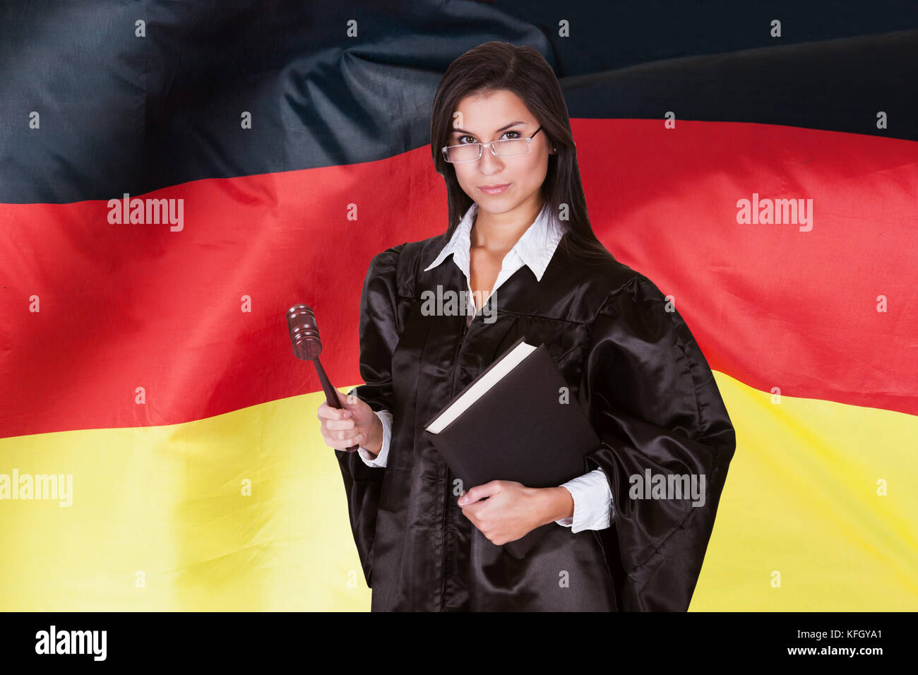 Confident Female Judge With Law Book And Wooden Gavel Standing In Front Of German Flag Stock Photo