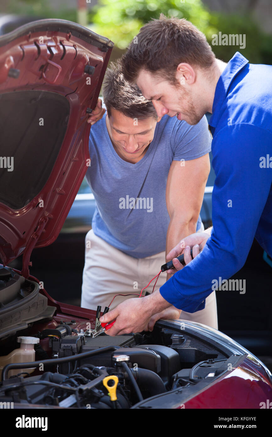 Male car owner with mechanic testing car battery outdoors Stock Photo