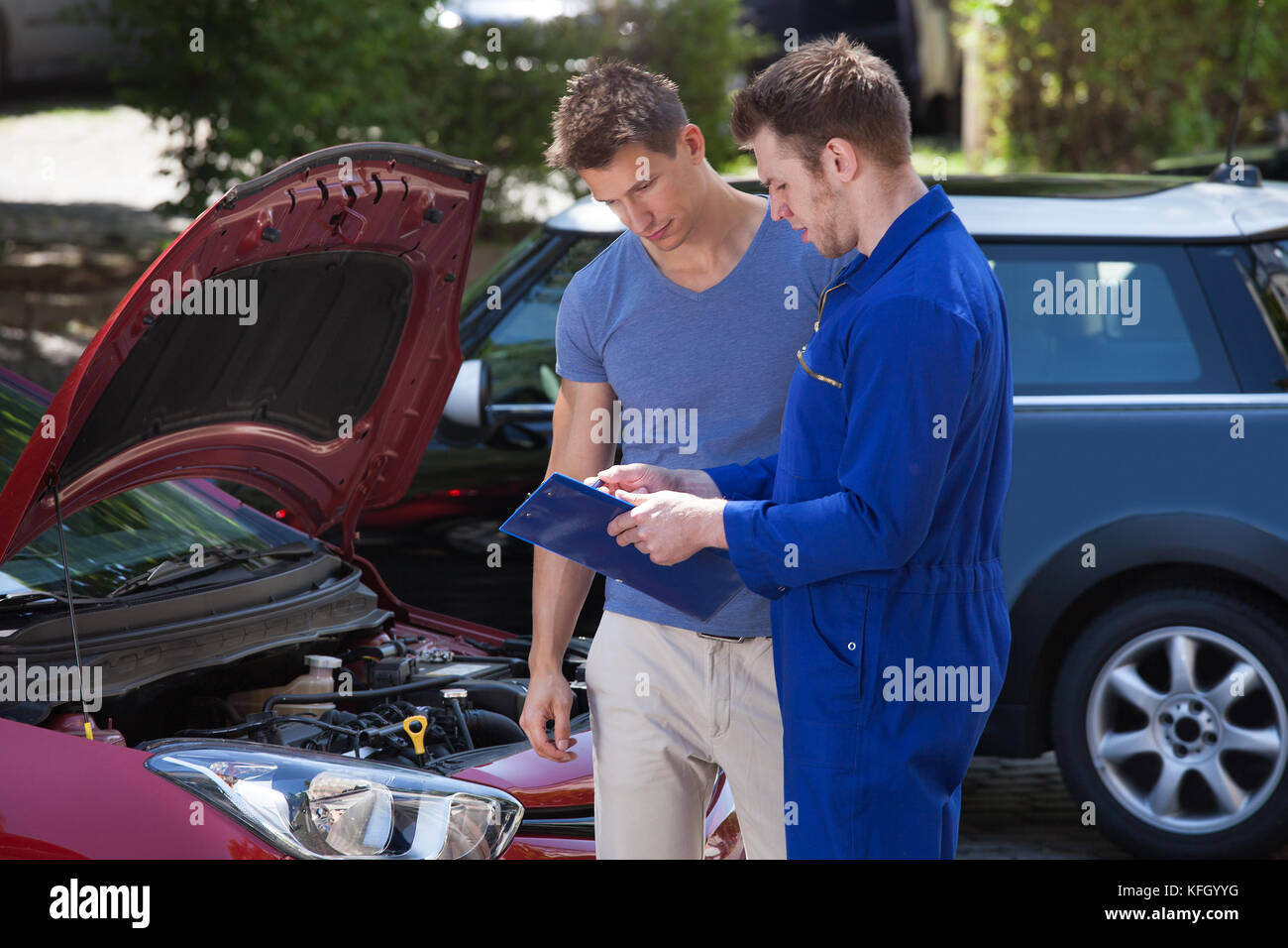 Young mechanic showing clipboard to customer by breakdown car Stock