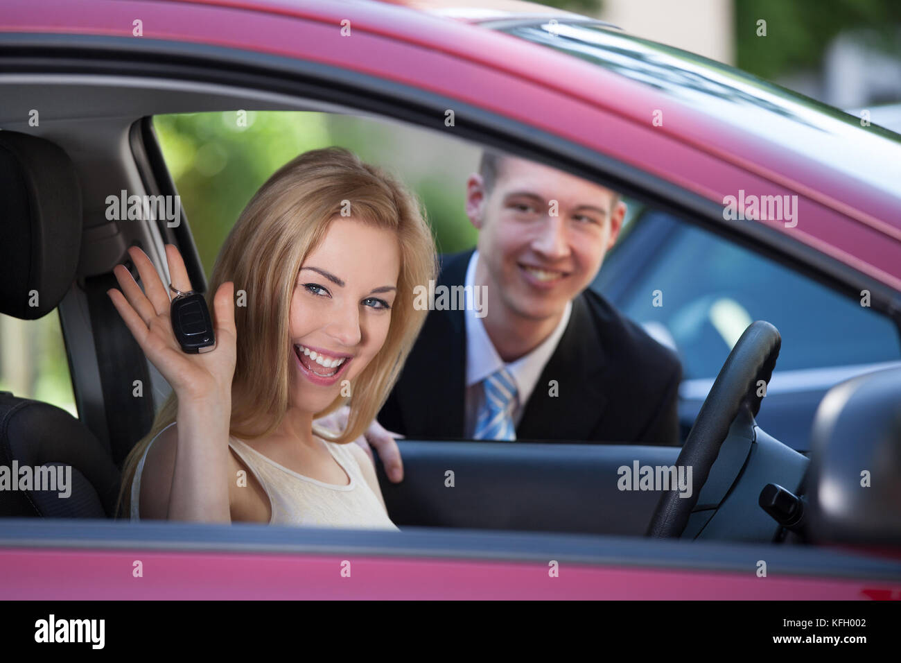 Portrait of happy woman showing key in car with salesman in background Stock Photo