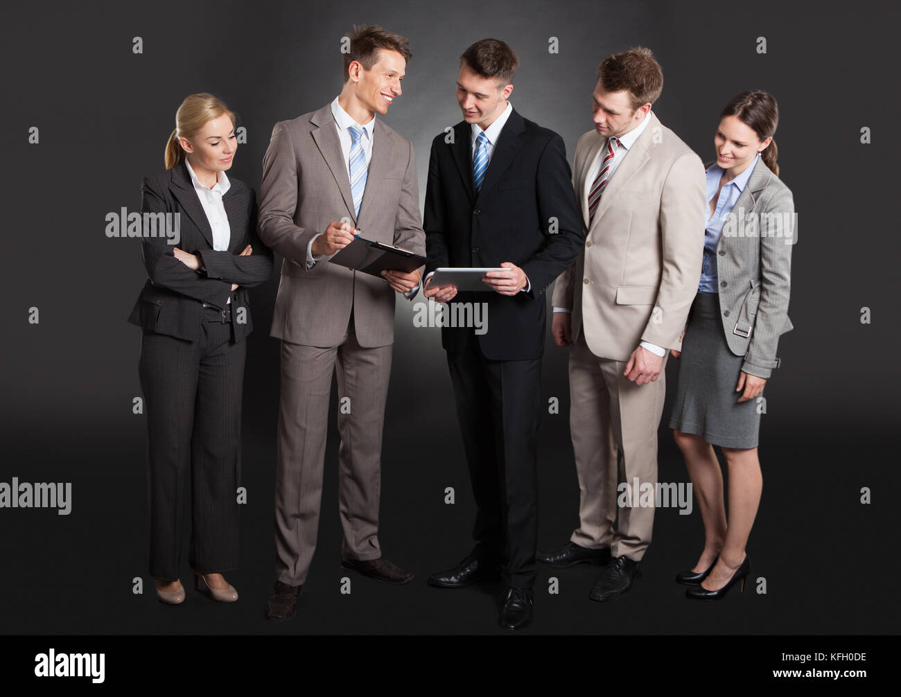 Happy business people discussing over clipboard while standing against black background Stock Photo