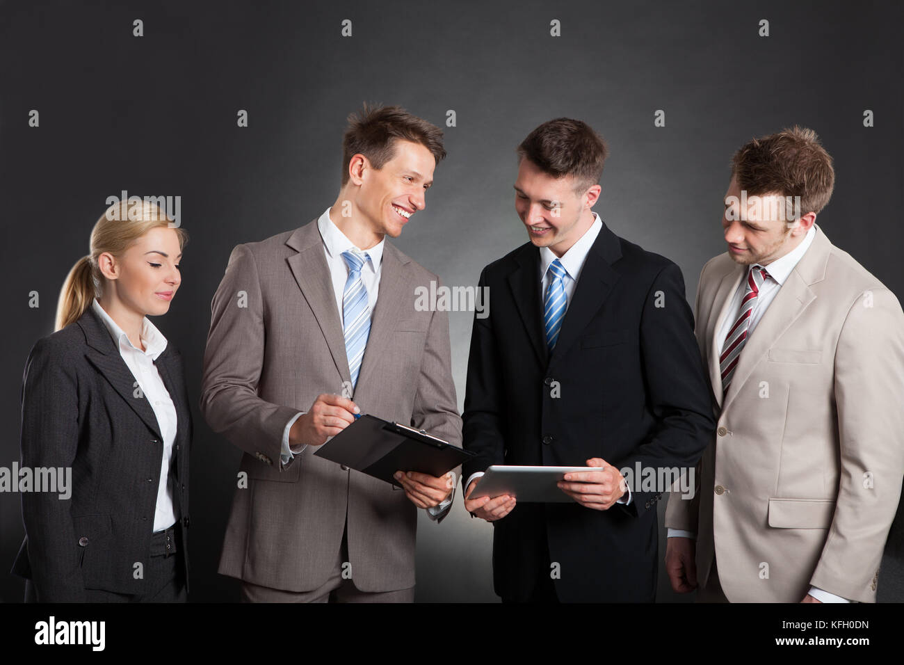 Happy business people discussing over clipboard while standing against black background Stock Photo