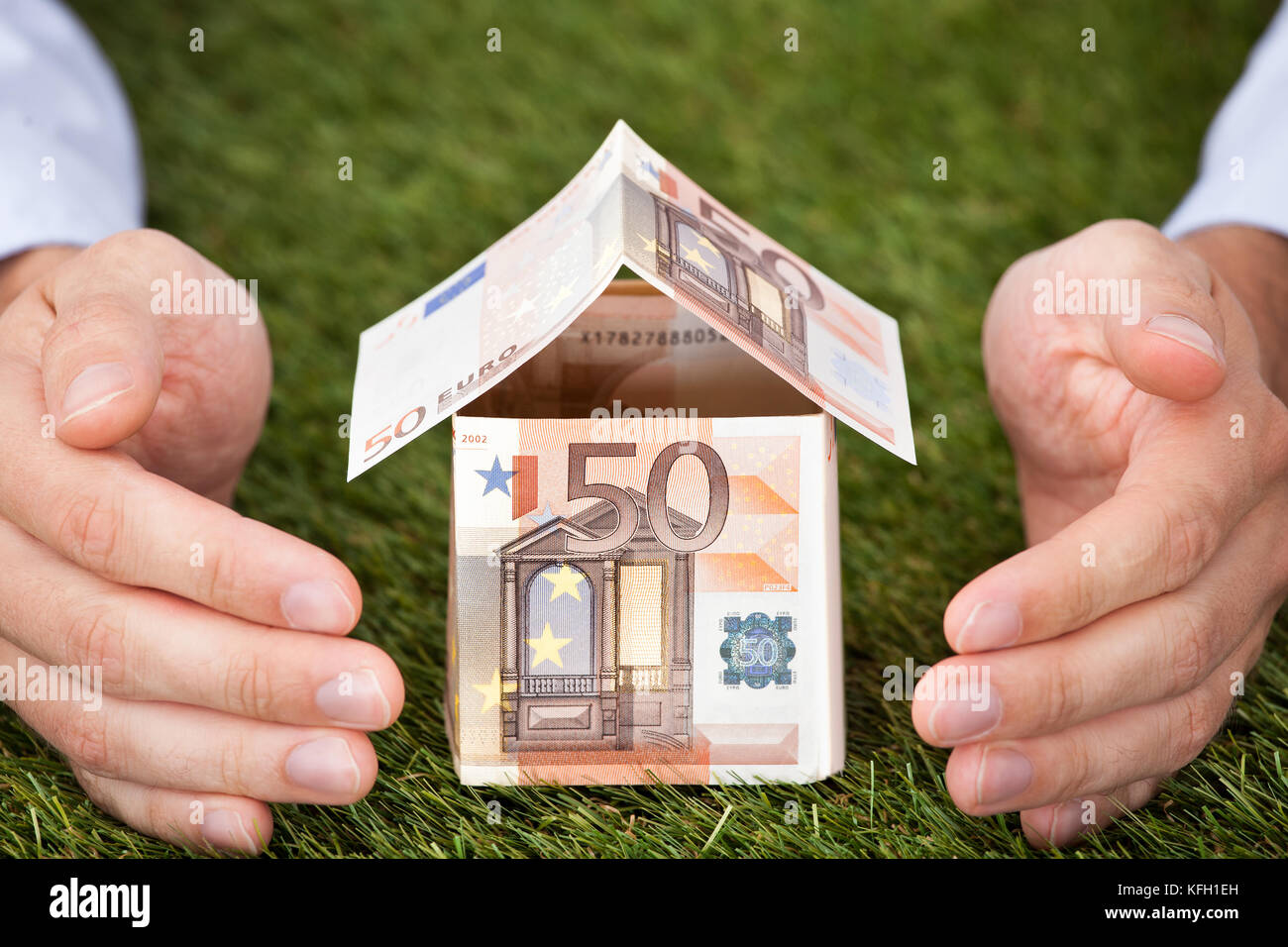 Businessman's hands protecting house made of euro notes on grassy land Stock Photo