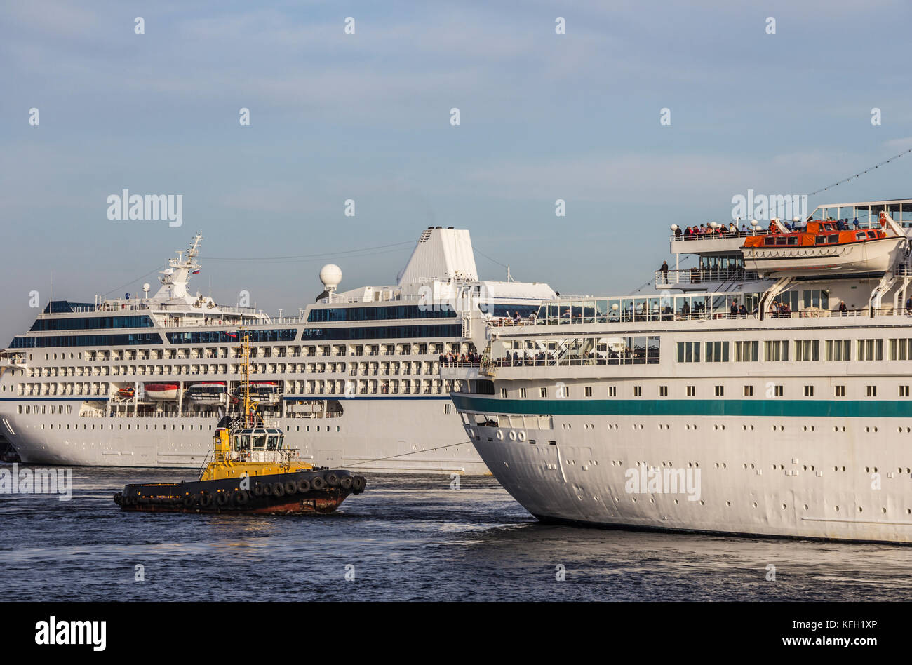 A huge cruise ships being manouvered and reversed towards high sea by pilots and tugboats Stock Photo