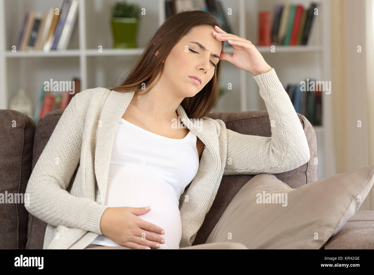 Pregnant woman suffering migraine sitting on a sofa at home Stock Photo