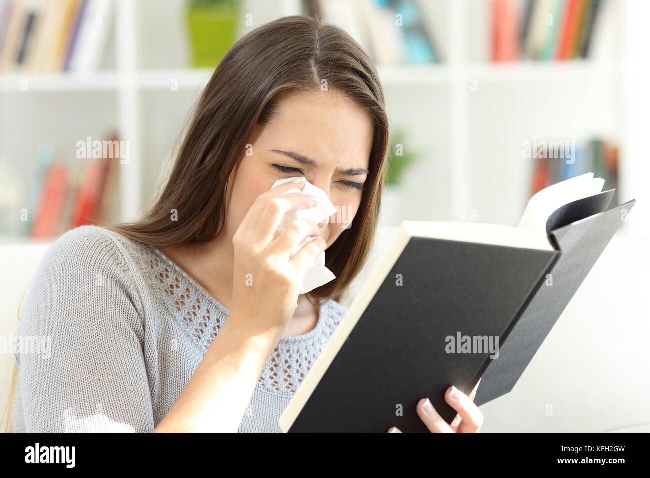Sad woman crying while is reading a good paper book sitting on a sofa at home Stock Photo