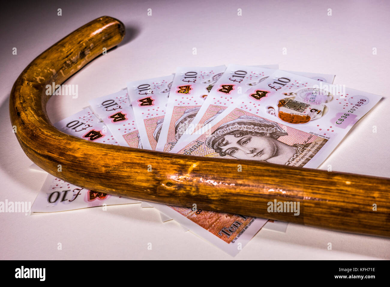 Walking stick / cane and new sterling £10 ten pound notes. Concept of link between old age and UK pounds, such as pension income and healthcare cost. Stock Photo